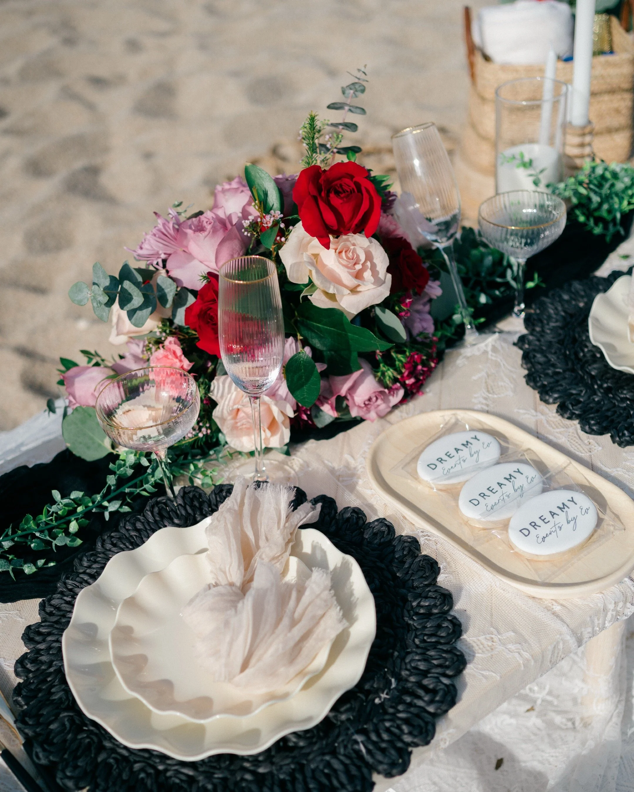 A decorated outdoor table with a floral centerpiece, champagne glasses, plates, and party favors with the word "DREAMY" on them.