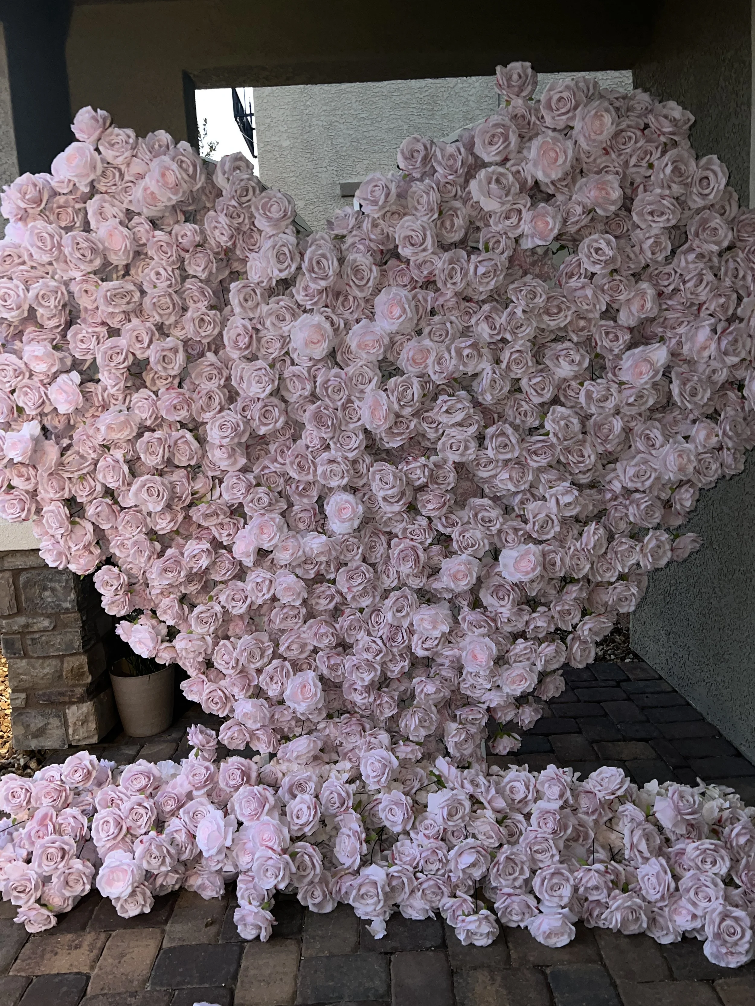 A large heart shape made of pink and white roses against a gray wall and outdoor patio with bricks.