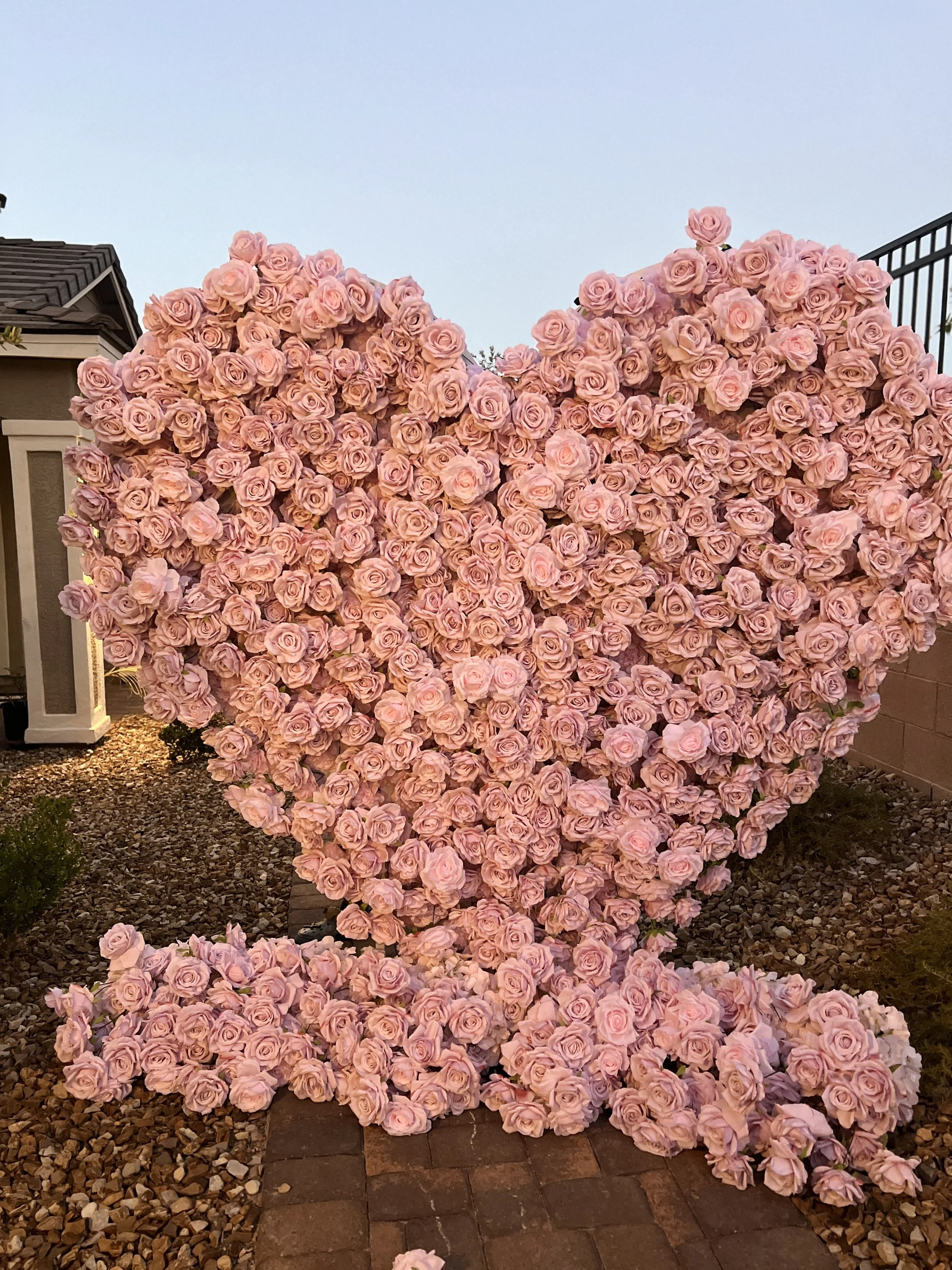 A large heart-shaped arrangement of pink roses outdoors on a brick pathway.
