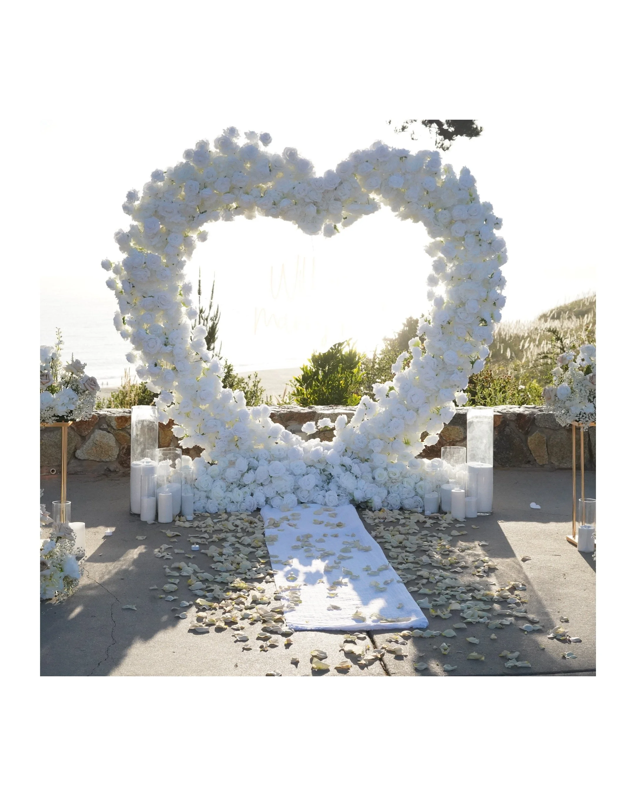White floral heart-shaped wedding arch with candles and flower petals on an aisle.