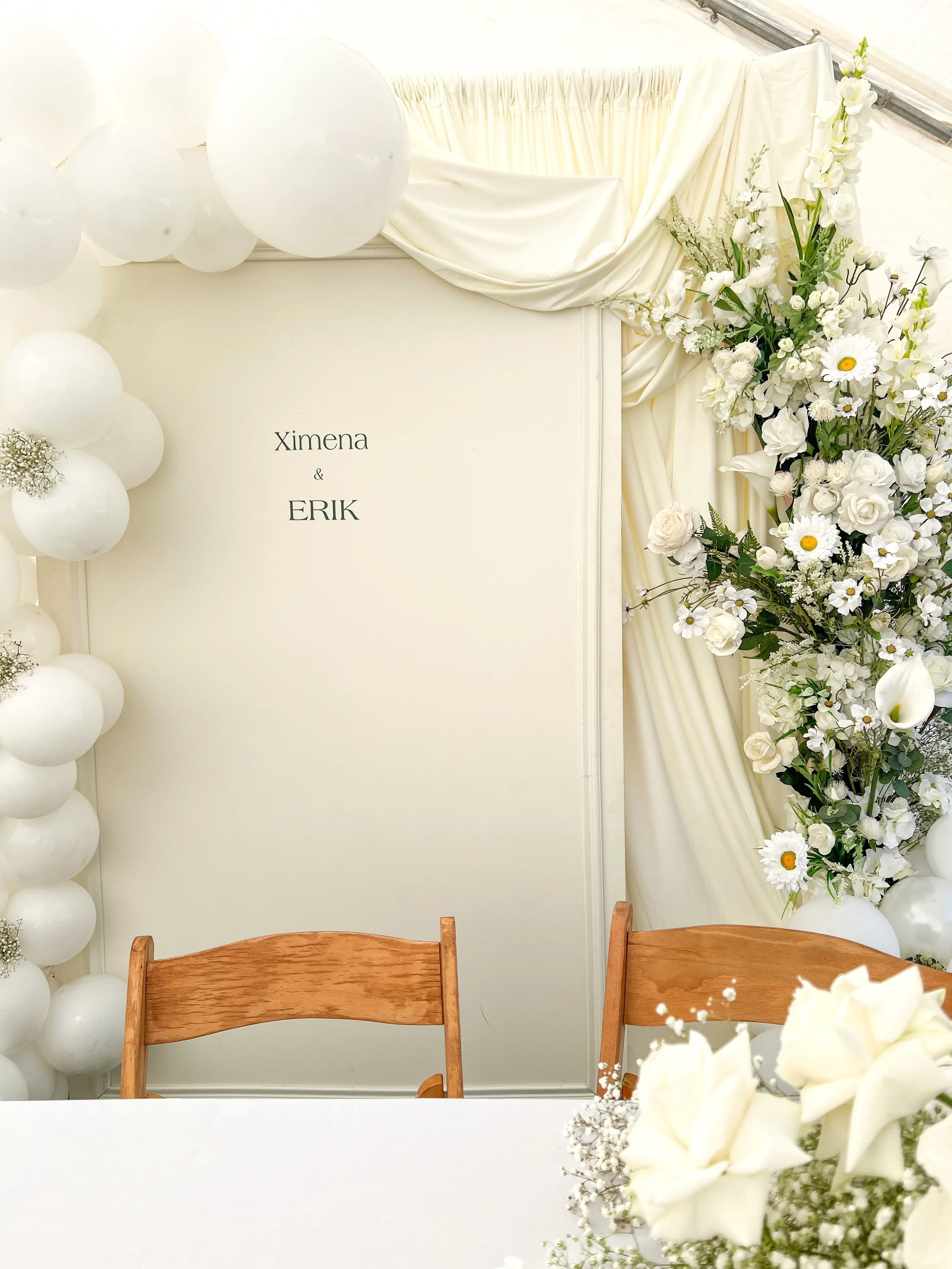 Wedding decoration with white flowers and balloons, featuring a sign with the names Ximena and Erik.