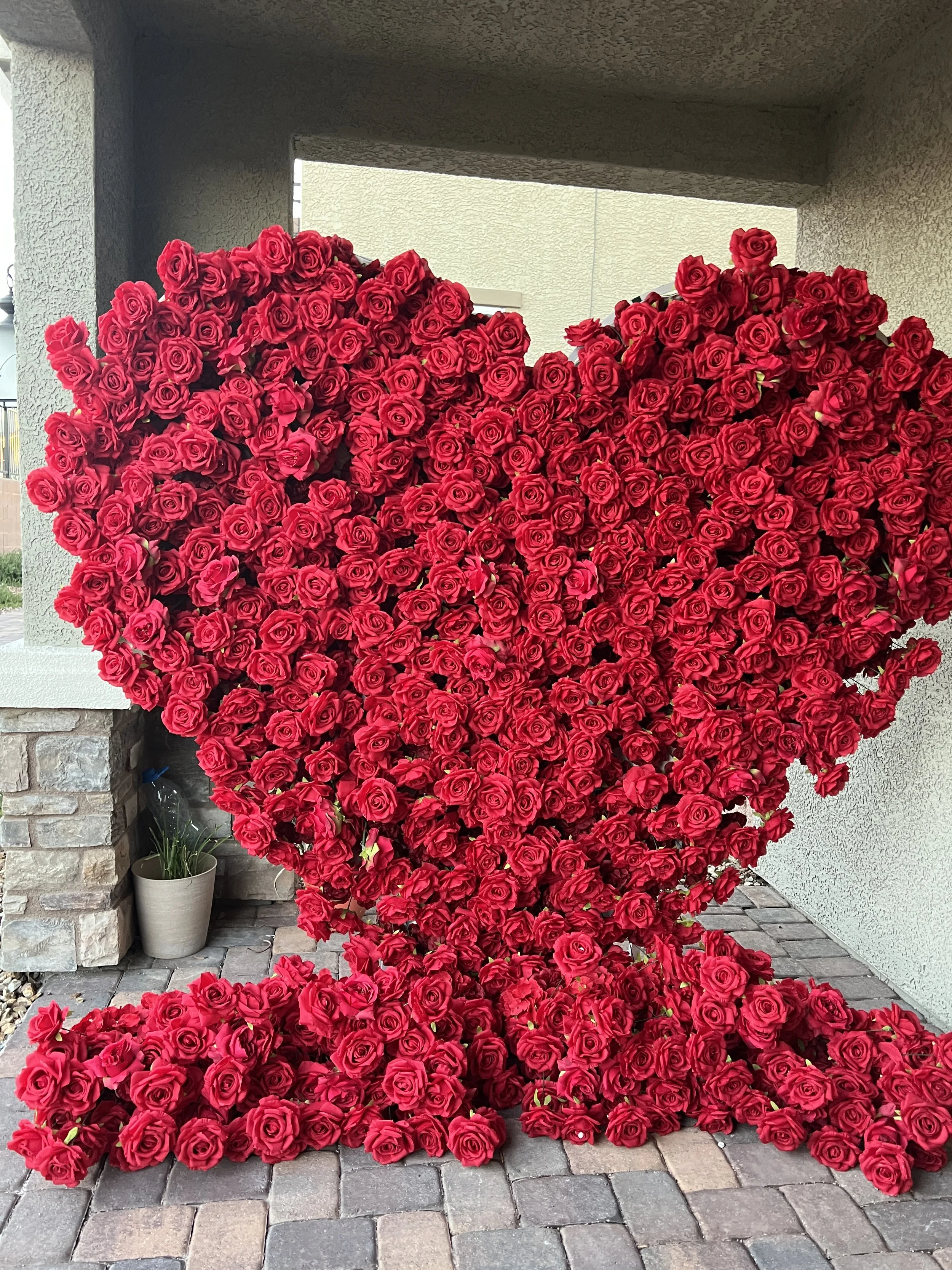 A large heart-shaped sculpture made of red roses placed outdoors on a paved surface next to a building.