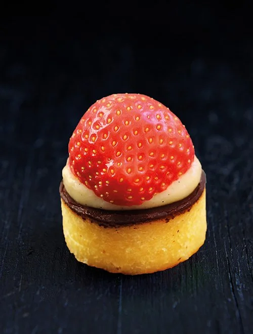 Lille dessert med jordbær, creme og chokolade på mørk baggrund.