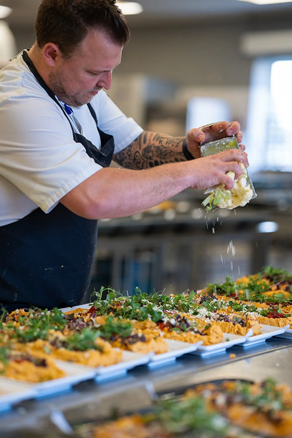 Firmafrokost fra Gastronomiet. Grønne serveringer med lokale råvarer og bælgfrugter. En kok med tatoveringer pynter fade.