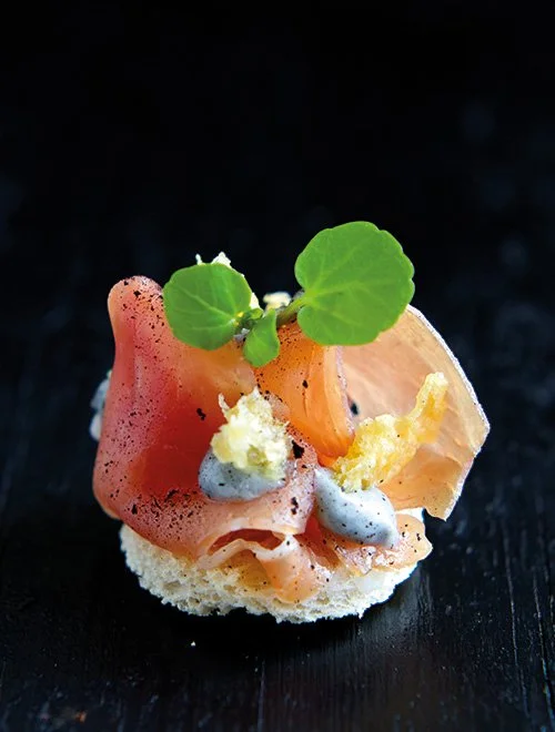 Gourmet forret med skiver af røget fisk, creme og grønt på en lille skive brød.
