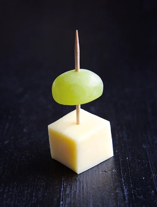 En tandstik med en grøn vindrue og en osteterning.