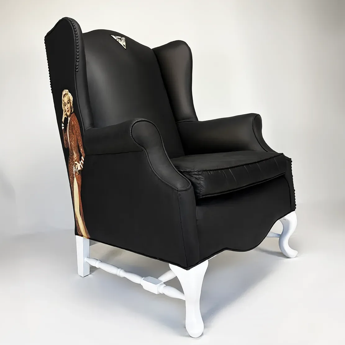Black armchair with white carved wooden legs and side panel featuring a vintage pin-up poster of a woman in a red dress.