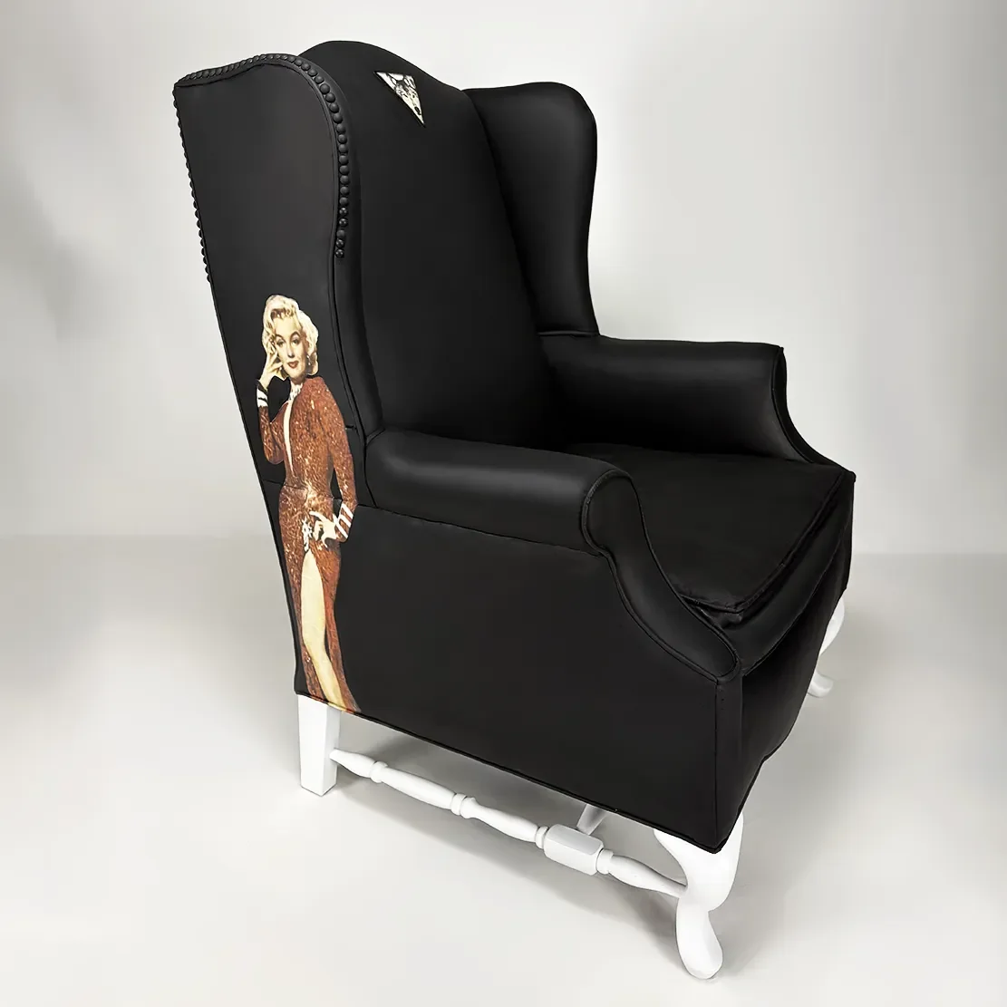 A black high-back armchair with white wooden legs, decorated with cutouts of Marilyn Monroe in a glamorous red dress on the side.