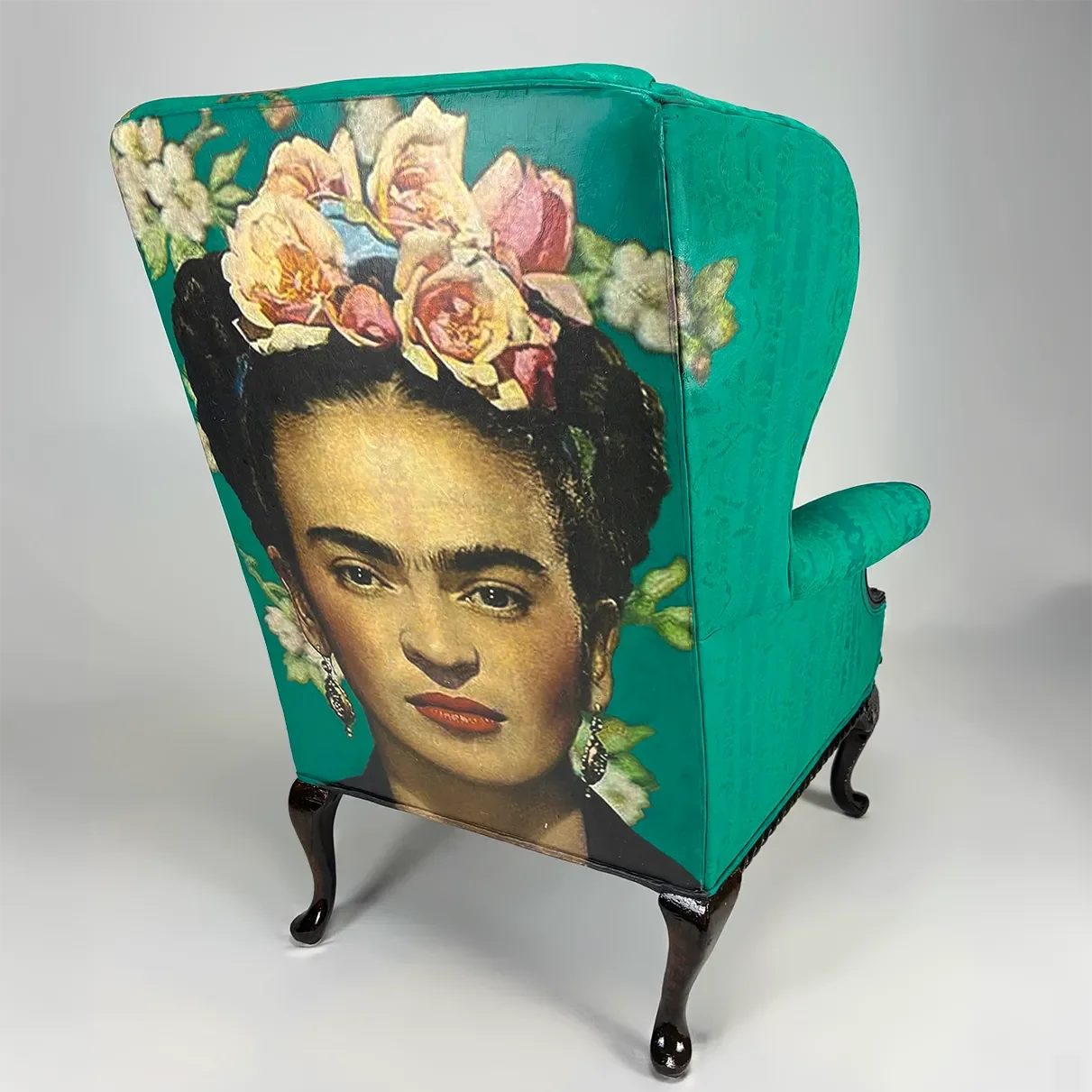 Decorative armchair with a portrait of Frida Kahlo and floral design on the upholstery, wooden legs with curved designs.