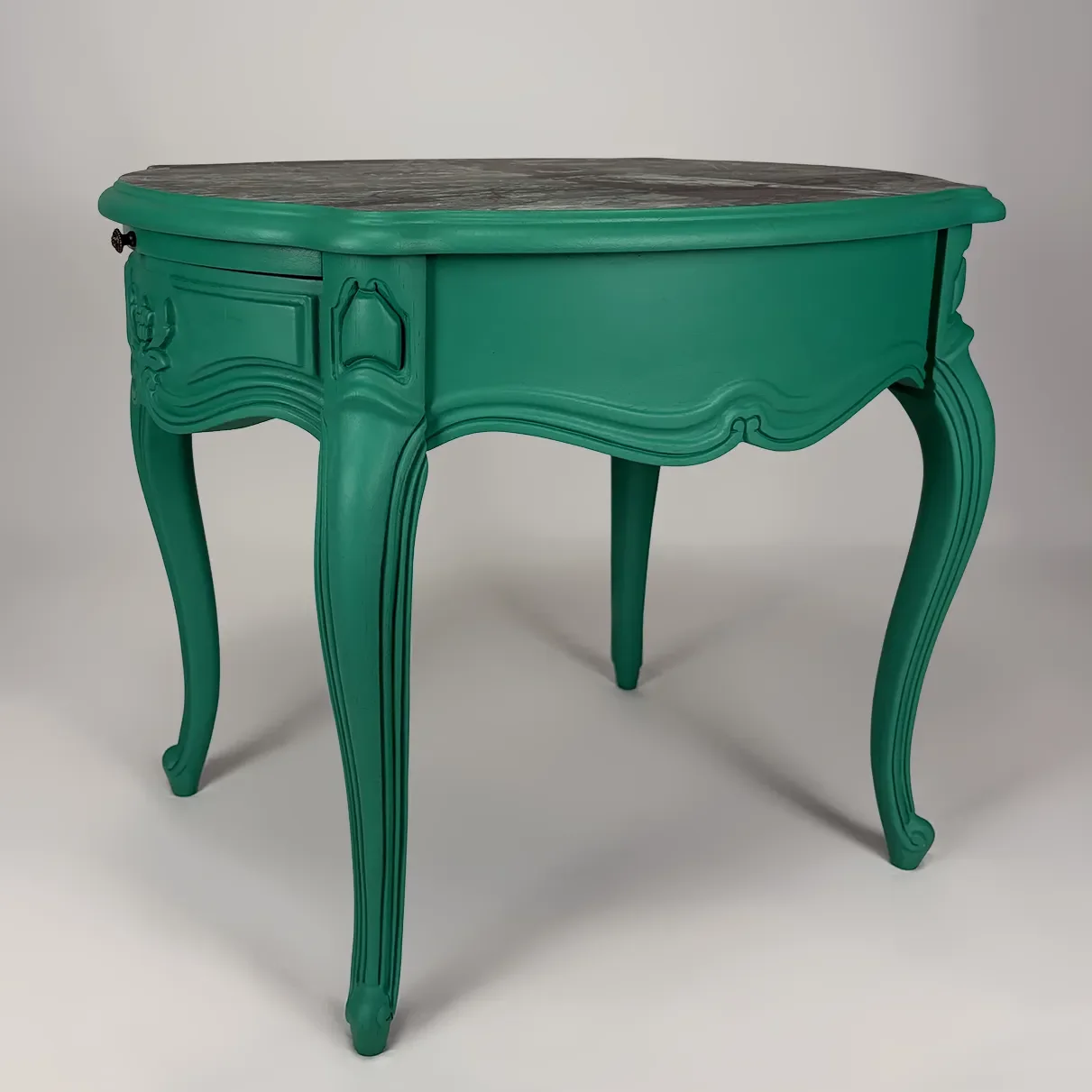 A vintage-style teal wooden table with ornate carved details and curved legs against a plain light background.
