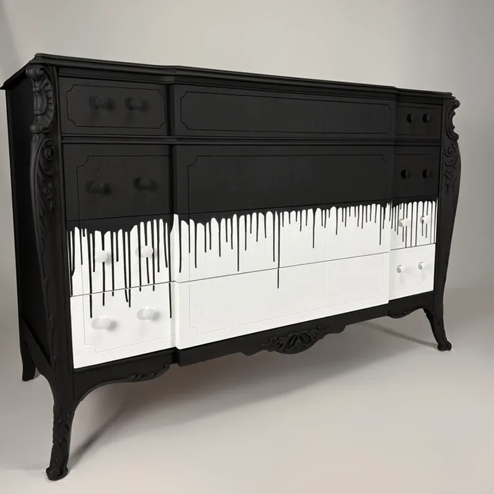 A black vintage-style dresser with ornate carvings, featuring drawers painted with black and white paint drip design.