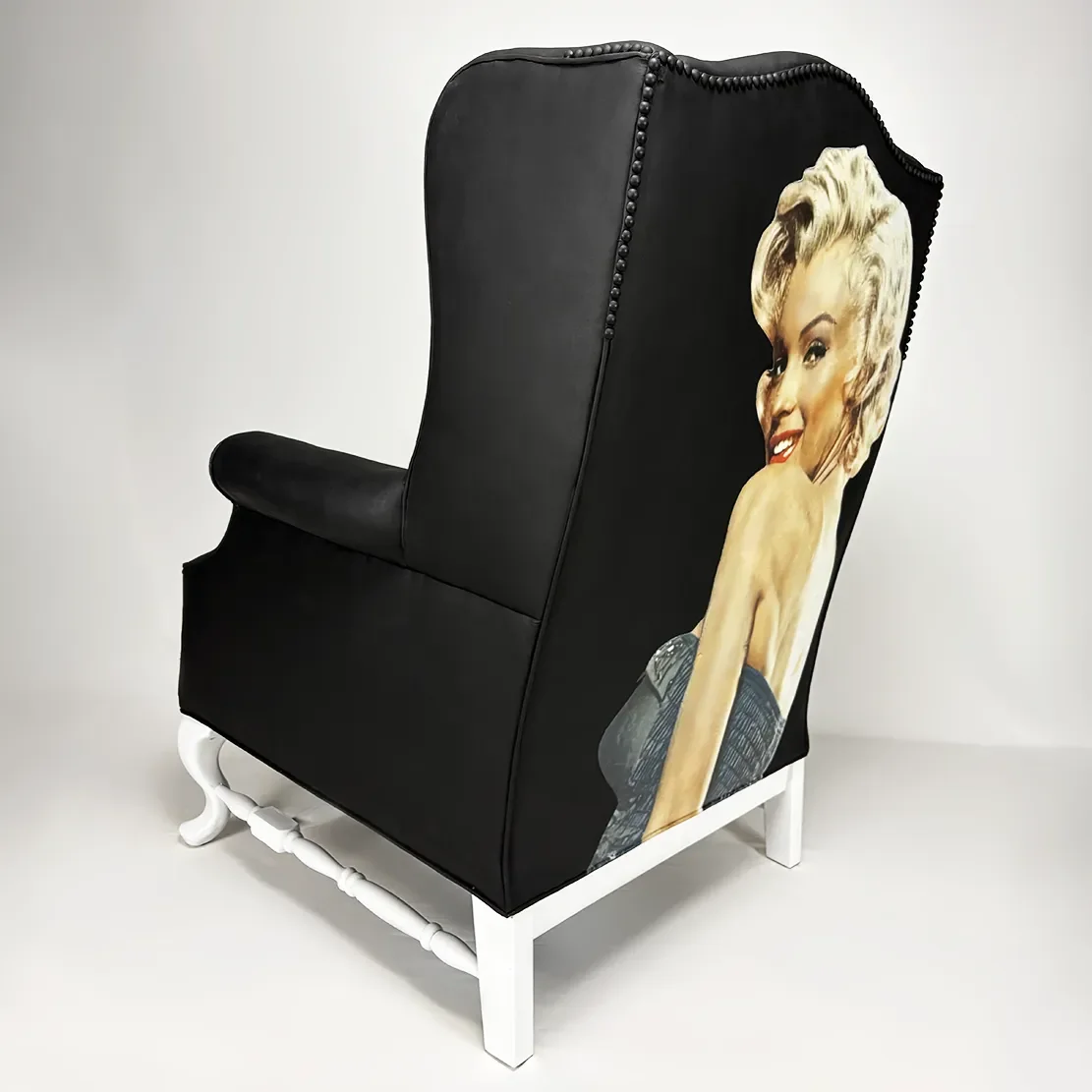 Black high-backed chair with white painted legs, featuring a painted portrait of Marilyn Monroe on the side.