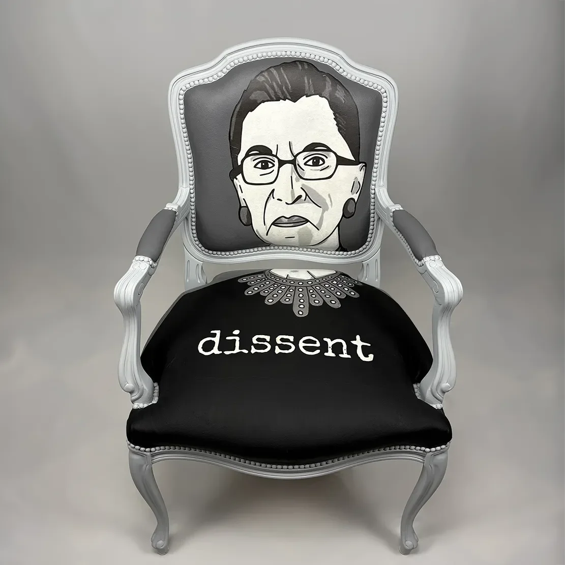 Decorative armchair with a painted portrait of Ruth Bader Ginsburg on the backrest and the word 'dissent' written on the seat