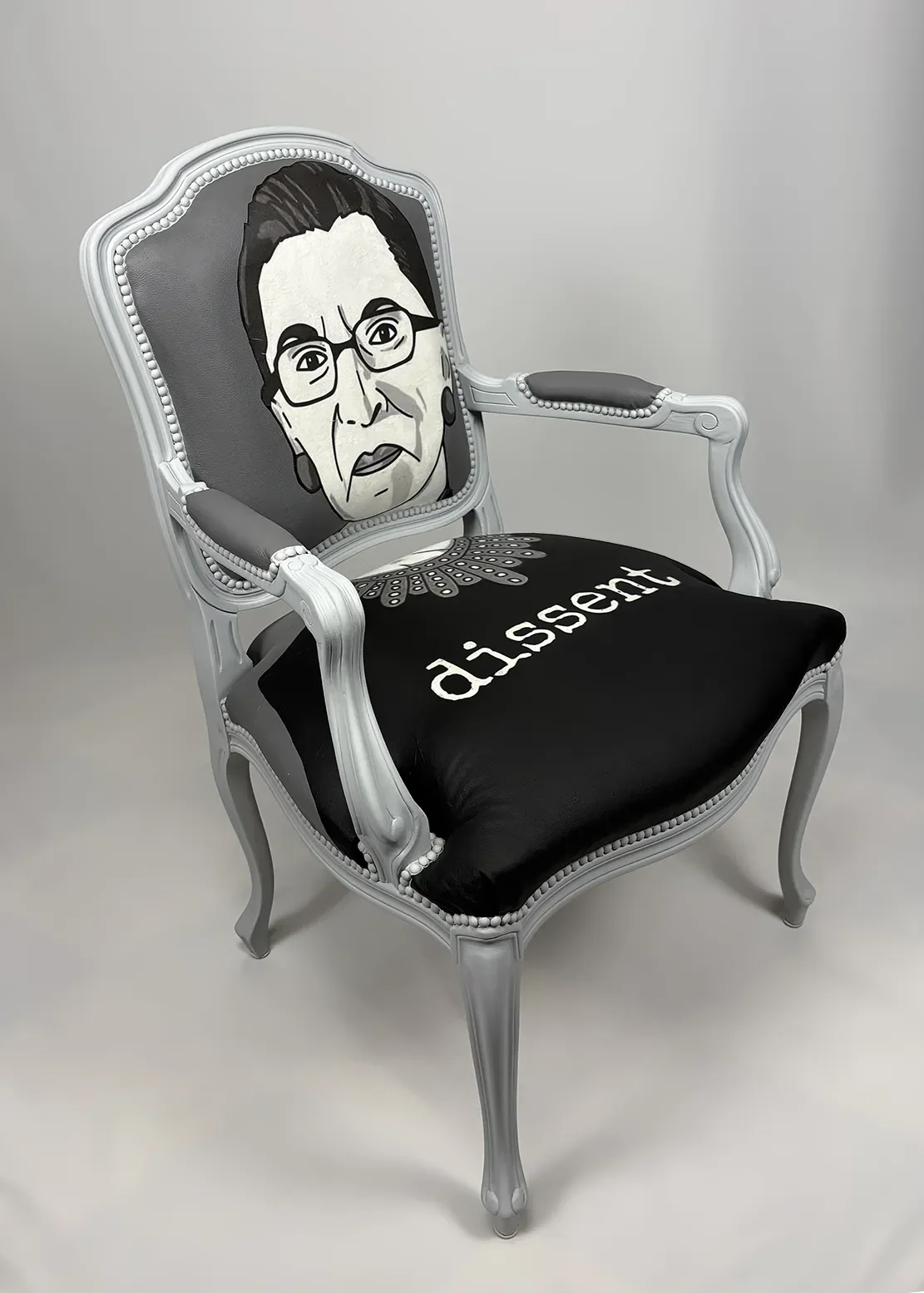 An ornate gray armchair with a portrait of Ruth Bader Ginsburg on the backrest and the word "dissent" written on the seat cushion.