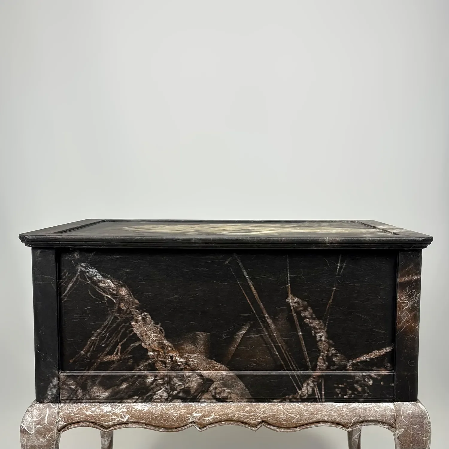 A vintage black and marble cabinet with floral and vine designs, placed against a light gray wall.