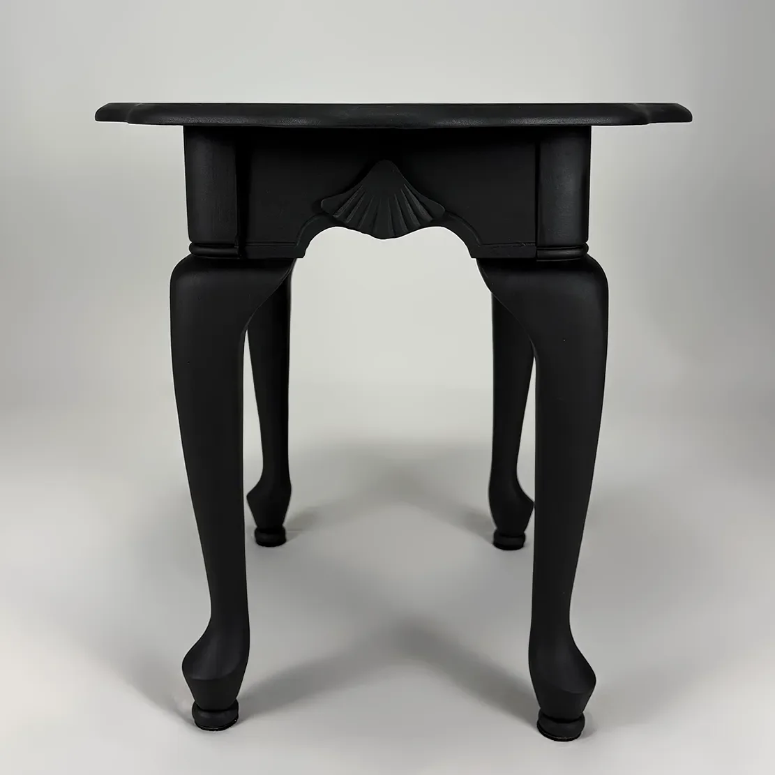 Black wooden table with curved legs and decorative carved detail on the front, set against a plain background.