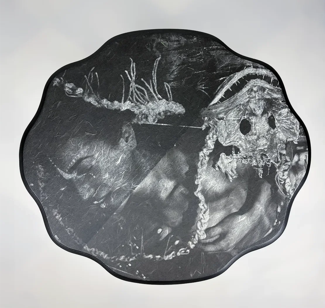 Black and white chalk drawing of a face with skeletal features and decorative elements, framed with a scalloped edge.