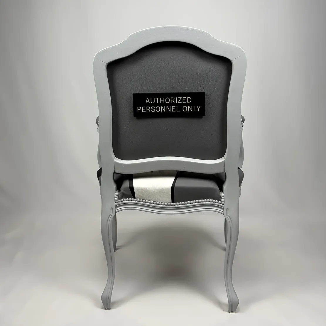 Elegant gray vintage chair with a black sign that reads 'Authorized Personnel Only' attached to the backrest, set against a plain gray background.