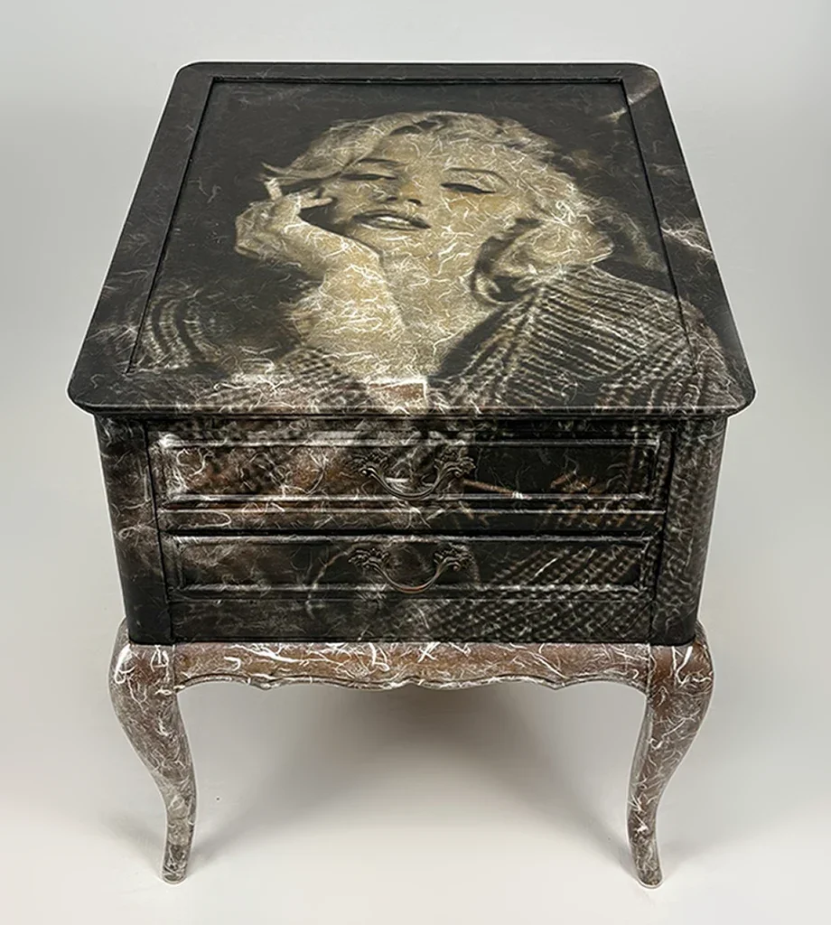 A small black and brown marbled furniture piece with a hinged lid and curved legs, featuring a vintage design.