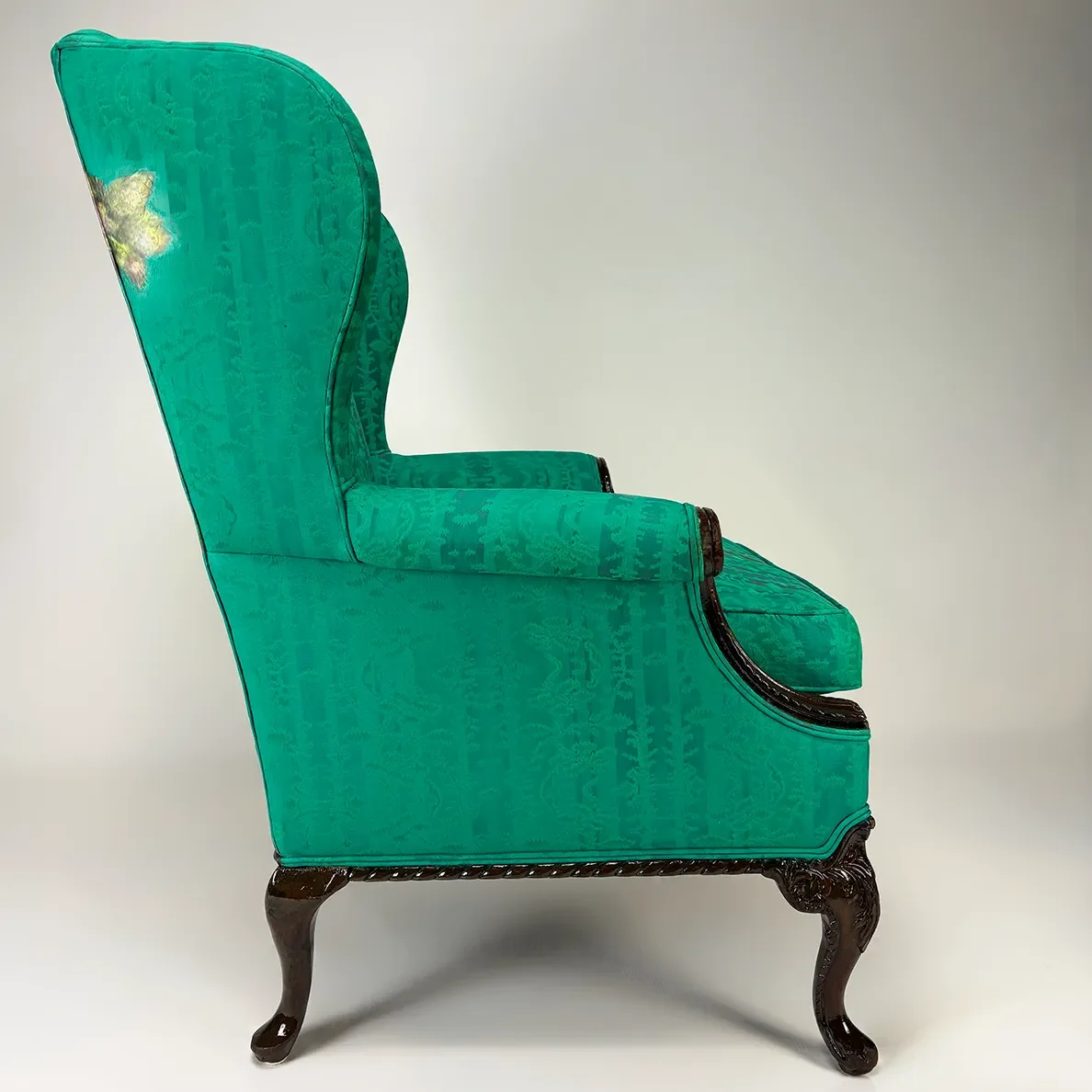 Side view of an antique Victorian-style armchair upholstered in teal fabric with dark wooden carved legs.