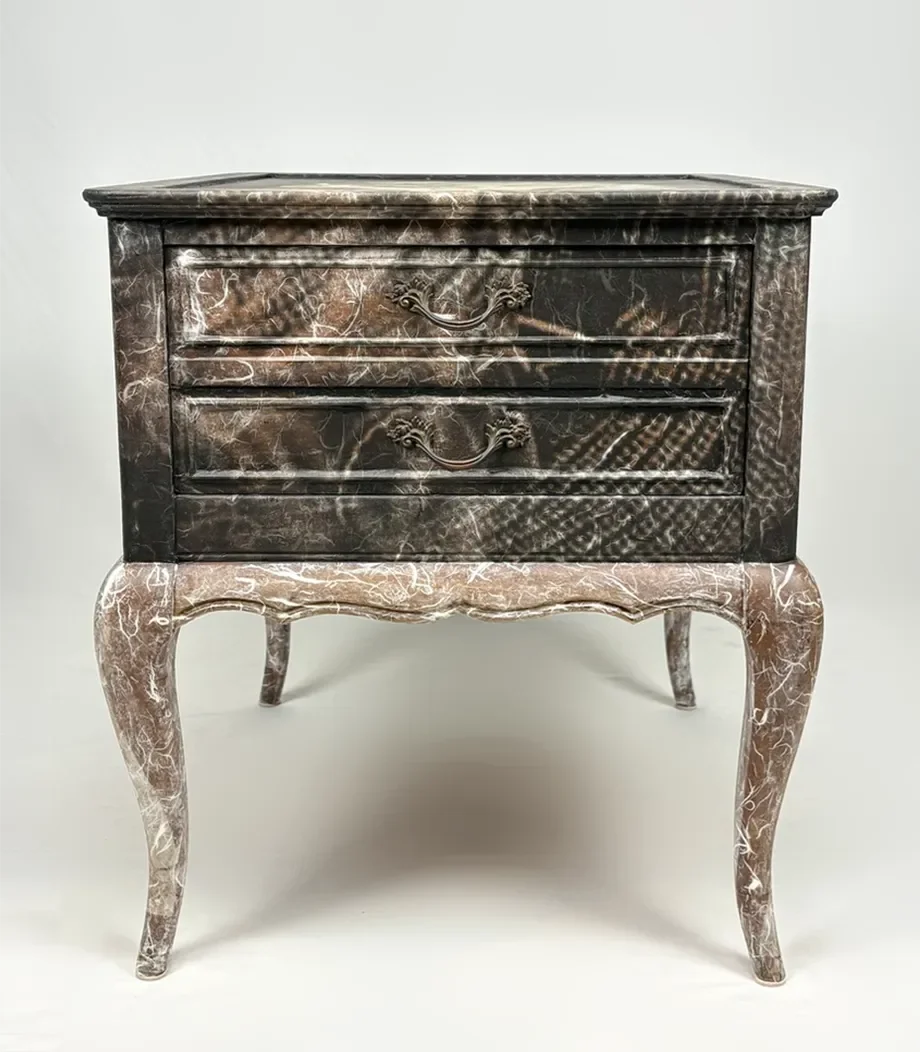 A vintage wooden dresser with two drawers, painted and distressed with a dark finish and ornate handles, standing on four curved legs.