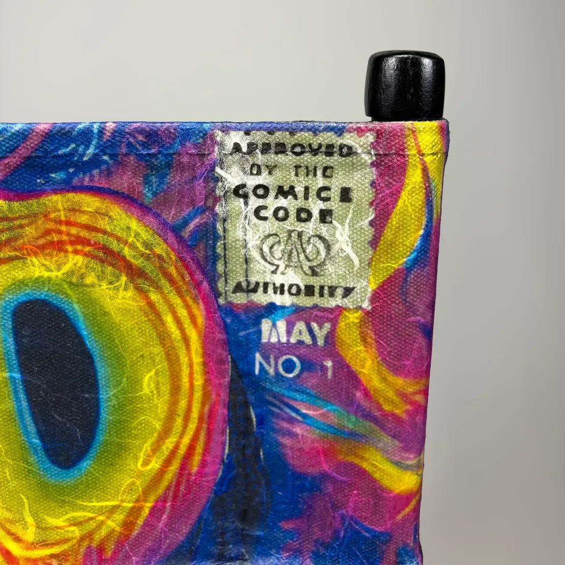 Close-up of a colorful, painted fabric with a UPC code sticker, partially torn, and a black plastic tube extending from the top edge.