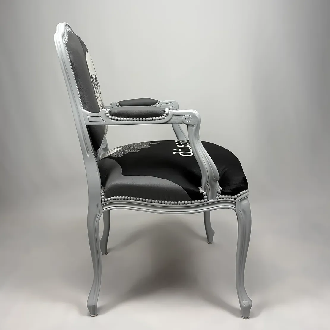 An ornate vintage armchair with a grey wooden frame, black upholstery, and decorative nailhead trim, placed against a plain white background.