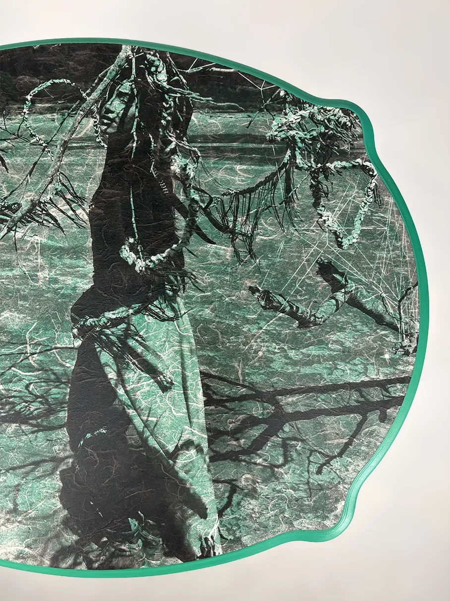 Close-up of a fabric with a printed image of a person outdoors, holding branches with leaves and cobwebs, surrounded by trees, with a green border.
