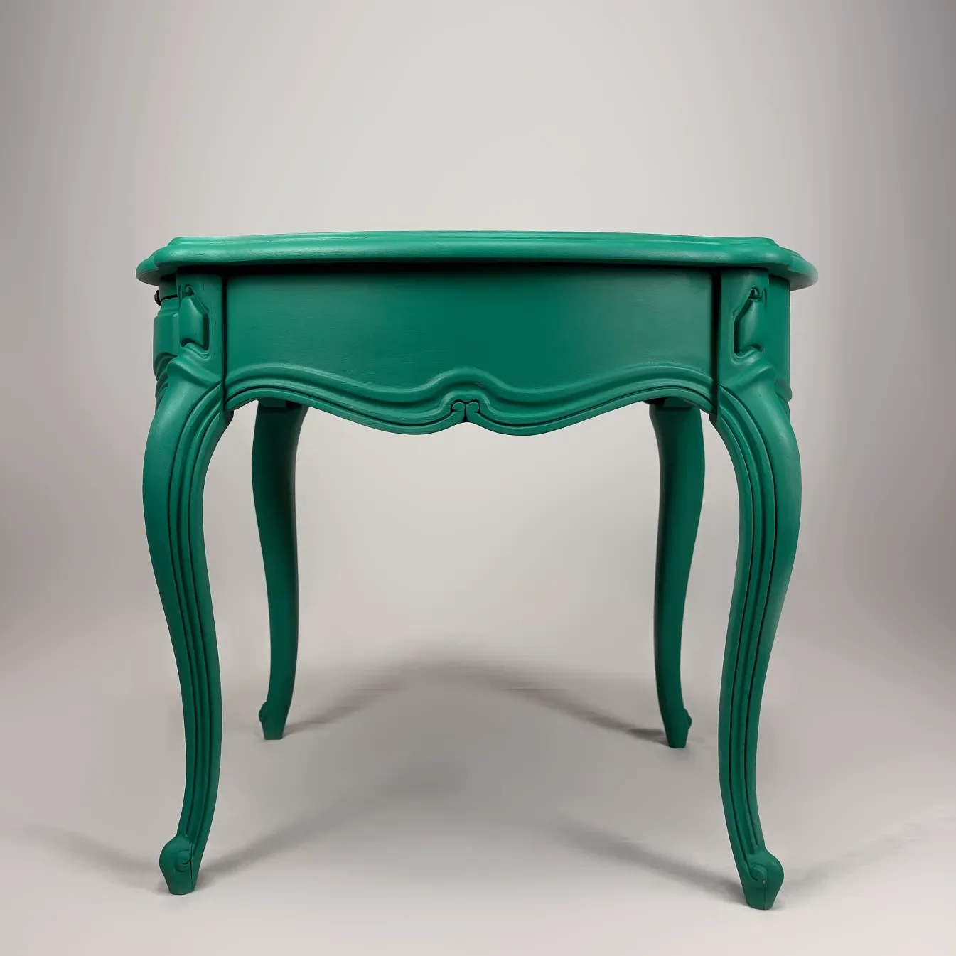 Green vintage-style wooden table with ornate curved legs on a plain background.