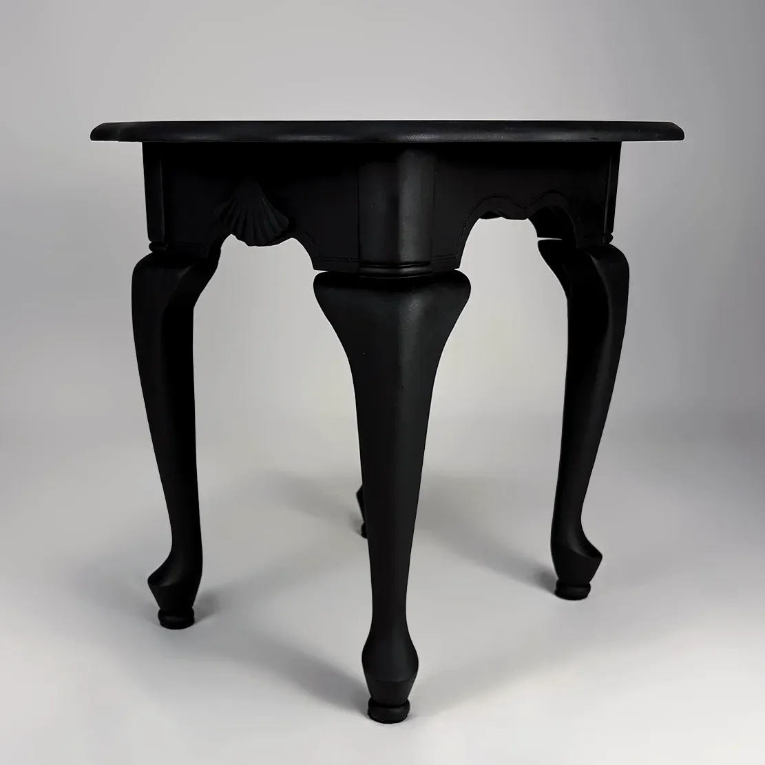 Black wooden table with curved legs and ornate details against a plain gray background.