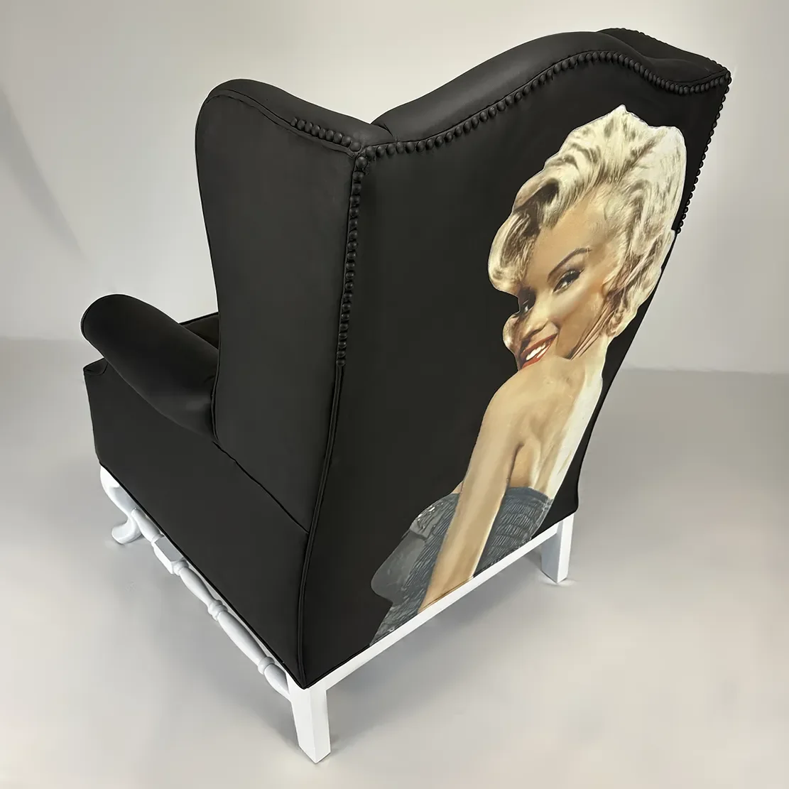 A black upholstered armchair with a vintage Marilyn Monroe poster on the backrest.