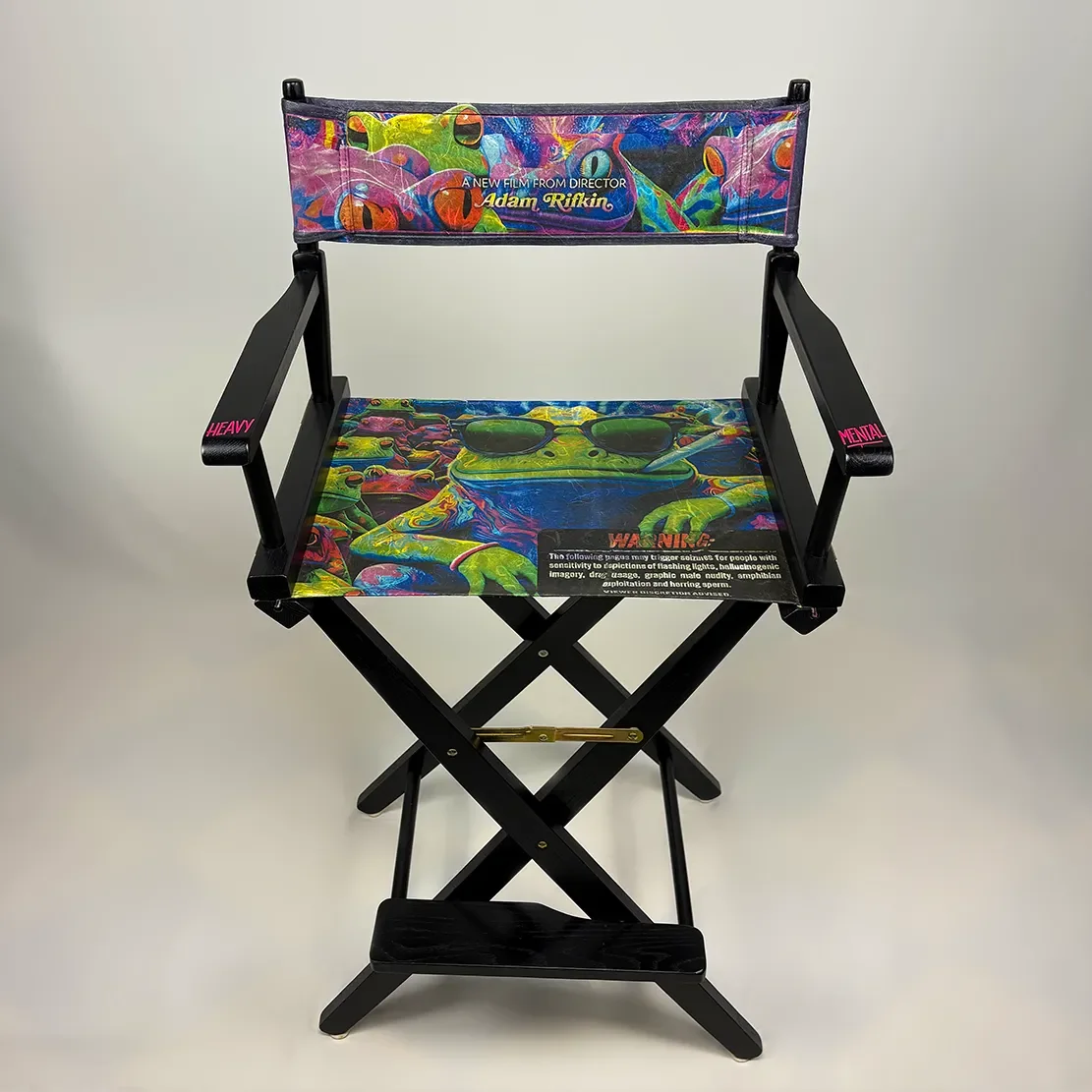 Colorful director's chair with psychedelic frog design and sunglasses pattern, featuring multiple warning labels on the seat and arms.