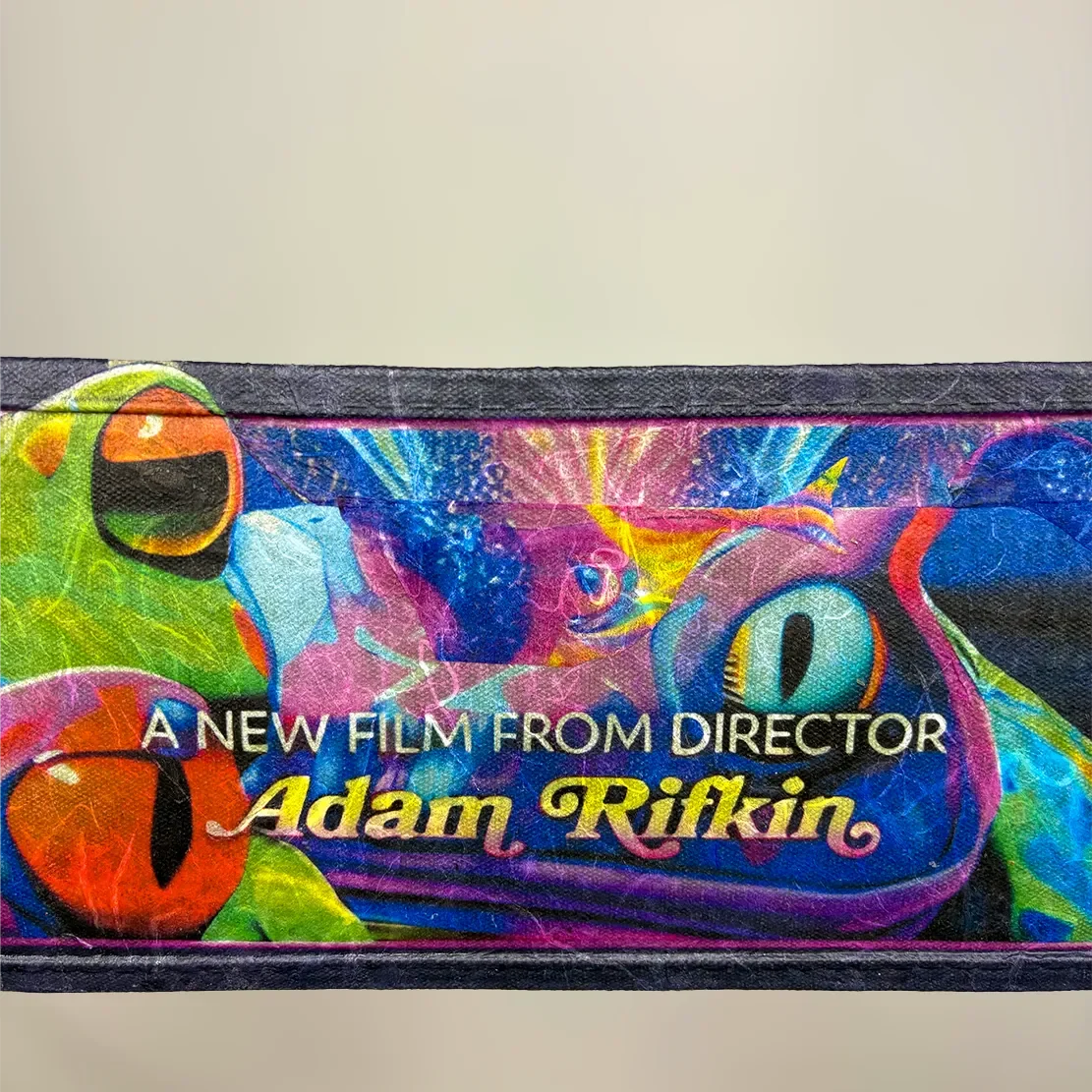 Close-up of a colorful promotional card with the text "A NEW FILM FROM DIRECTOR Adam Rifkin" and bright, neon-colored abstract designs and shapes.