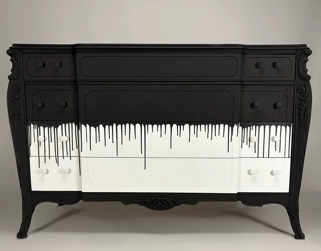 Black vintage dresser with paint drip design that appears as black paint dripping down white drawers, set against gray background.