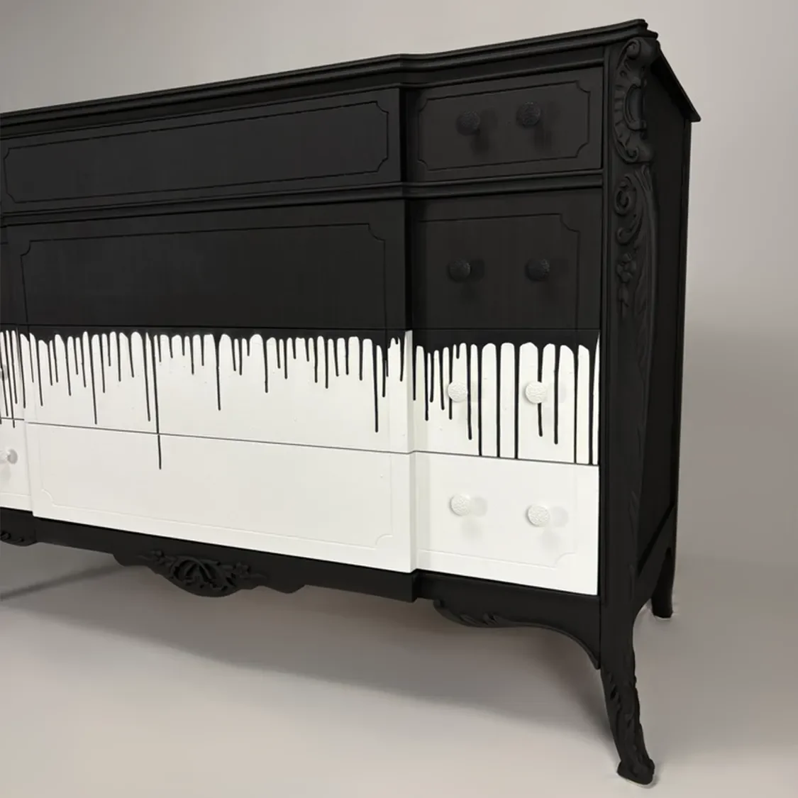 A black and white dresser with paint dripping from the top black portion onto the white bottom part, creating a dripping paint effect.