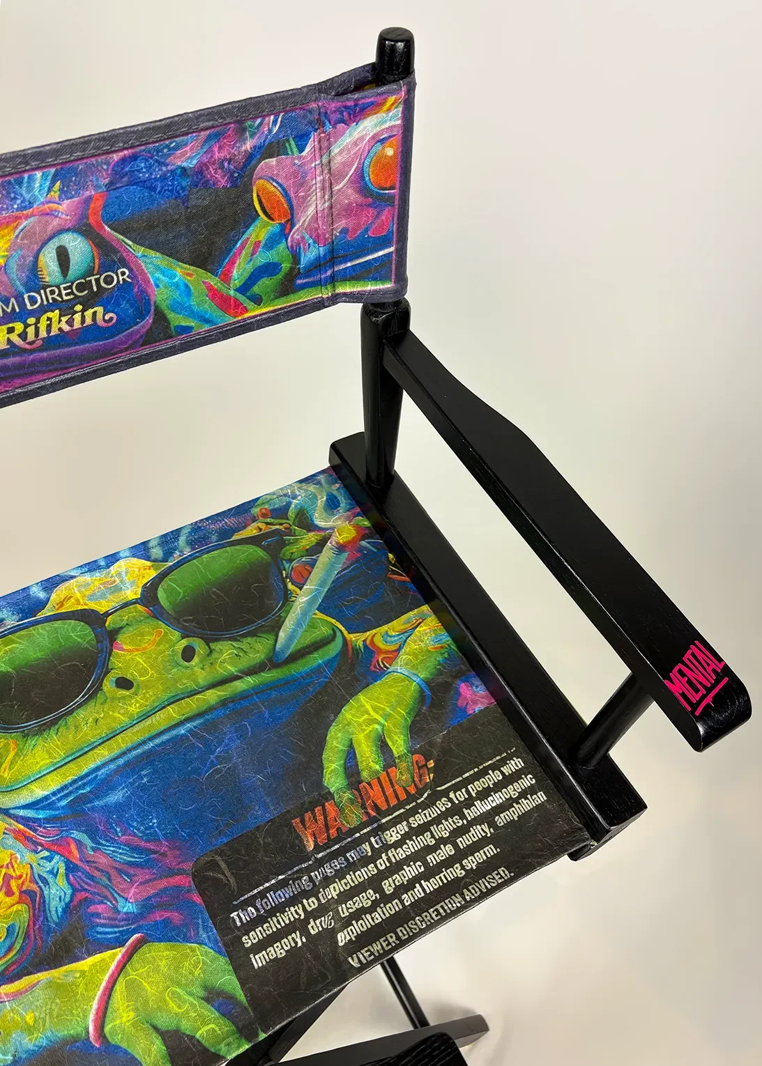 Close-up of a colorful director chair with a handcrafted decoupage print of "TOAD" movie poster, and a sticker 'MENTAL' on the armrest.
