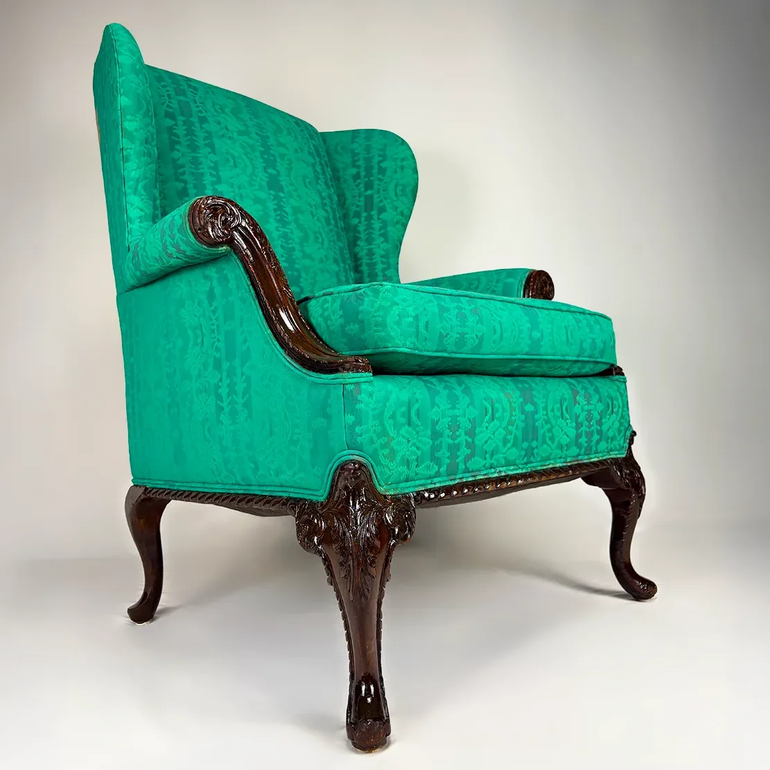 A vintage upholstered armchair with a high back, bright teal fabric, and dark wooden carved legs and armrests.