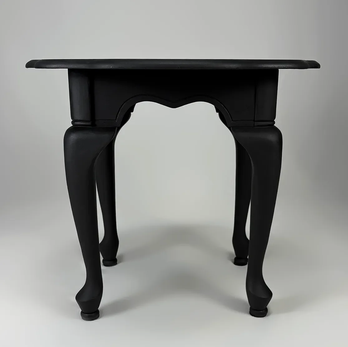 A black wooden table with curved, ornate legs against a light gray background.