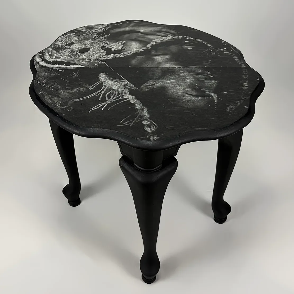 A small black table with a rounded, scalloped edge top featuring white marbled patterns and legs in a cabriole style.