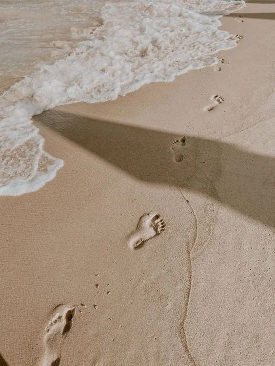 Footprints in the sand along a shoreline with gentle waves washing up.