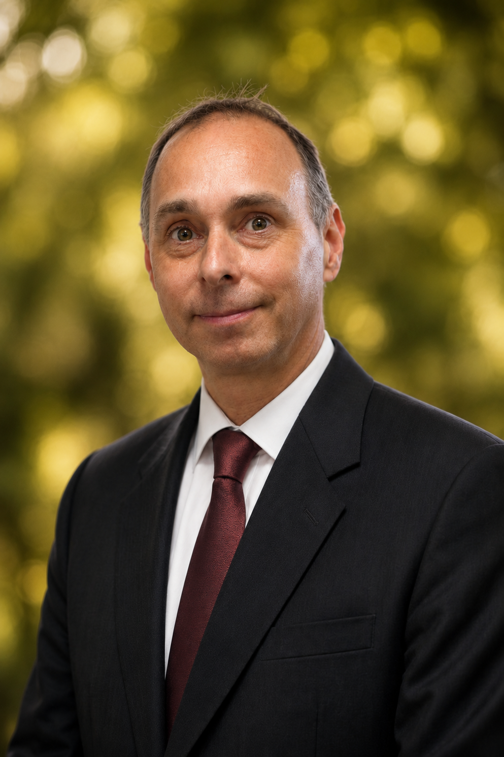 Man in a suit with a tie standing against a dark gradient background.