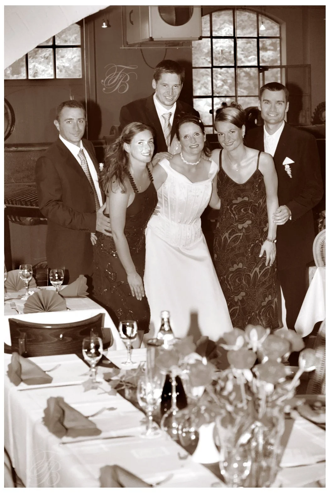 Eine Gruppe von sechs Menschen, drei Männer und drei Frauen, posieren bei einer Feier in einem schön dekorierten Raum. Die Frauen tragen elegante Kleider, die Männer tragen Anzüge.