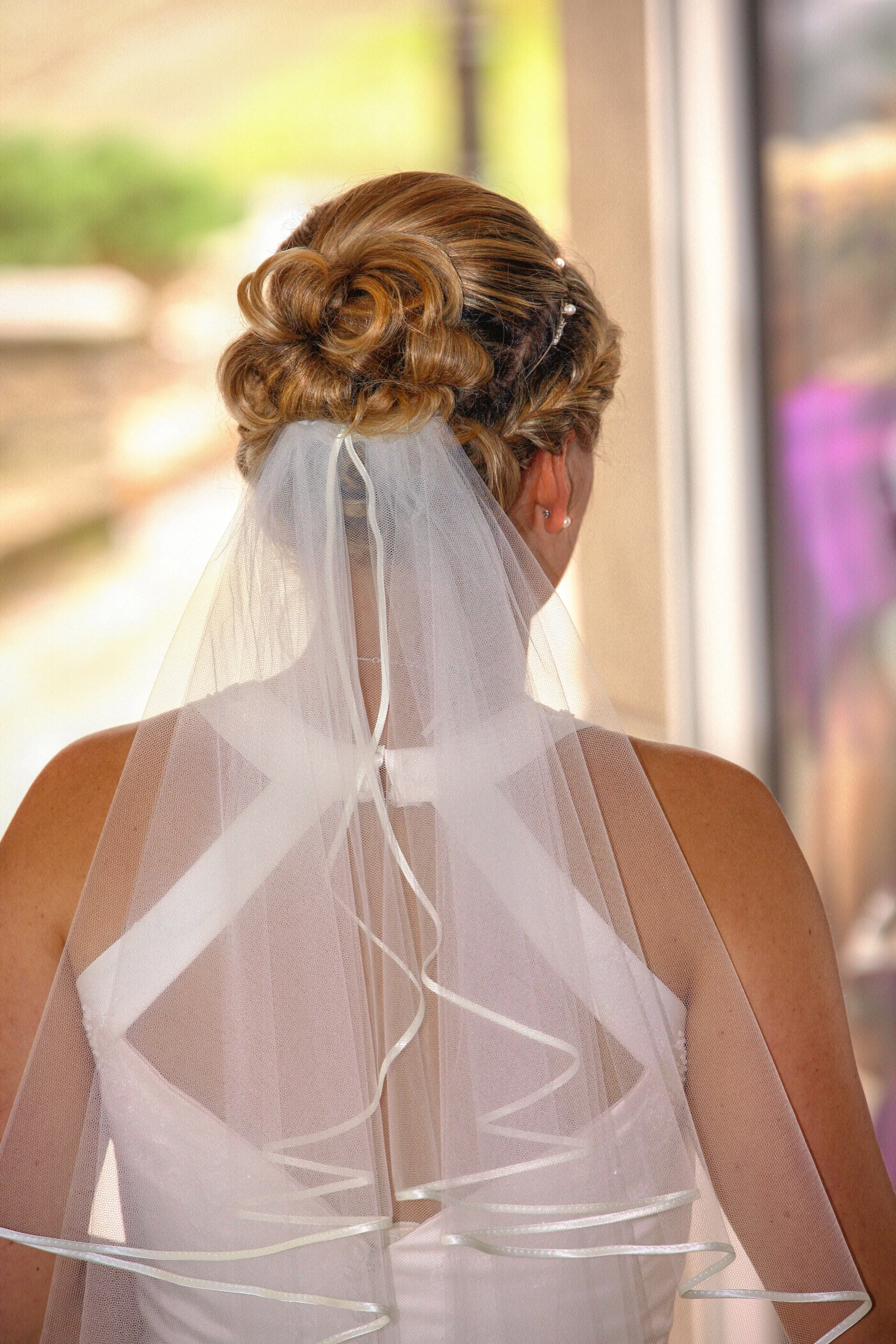 Eine Frau mit elegant frisiertem Haar in einem Brautkleid und Schleier, die wahrscheinlich eine Braut ist.