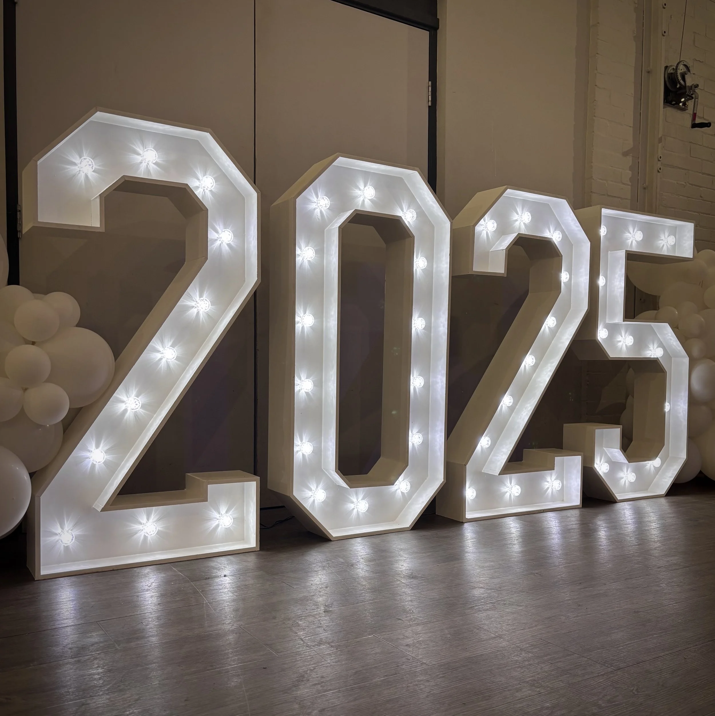 Illuminated marquee numbers reading 2023, decorated with white balloons on the side.