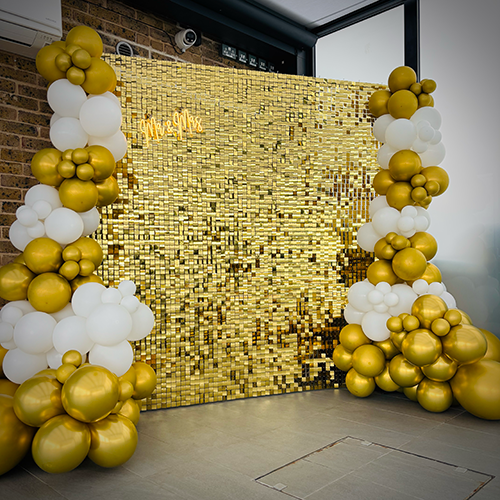 Gold shimmer wall with gold and white balloons and 'MR&MRS' LED sign for a wedding at St Ive s Golf Club