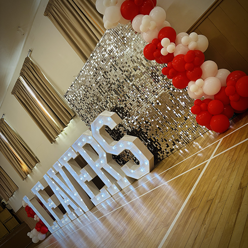 Silver shimmer wall with light up "LEAVERS" and white and red balloon decor for Thaxted Primary School in Essex