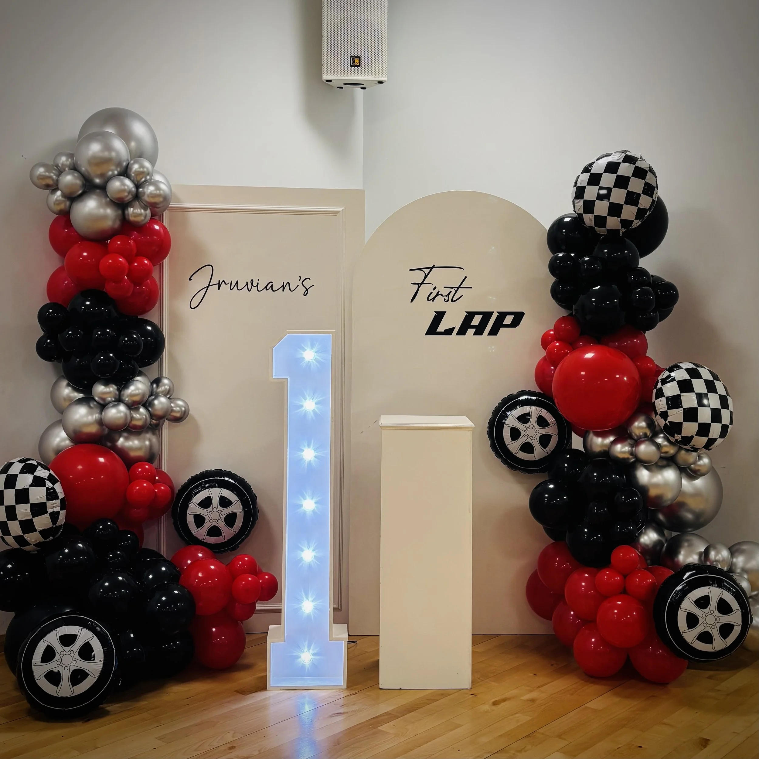 A white backdrop with red cursive text that says 'I was always you', decorated with a cluster of white balloons on the left side, in a room with wooden furniture, curtains, and large windows showing a golf cart and trees outside.