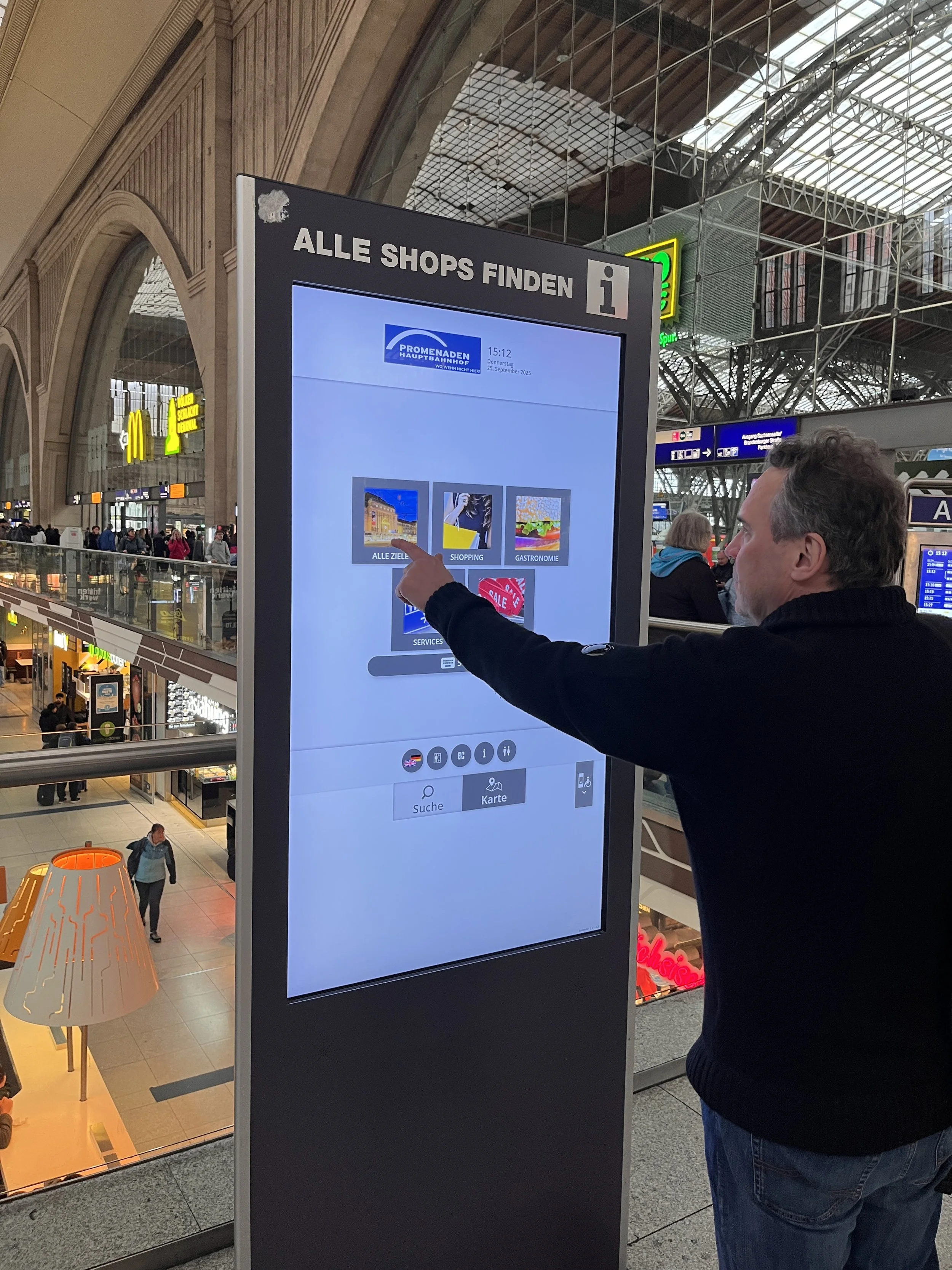 Ein Mann bedient einen digitalen Infostand im Hauptbahnhof, um Geschäfte, Gastronomie, Service und alle Ziele zu finden.