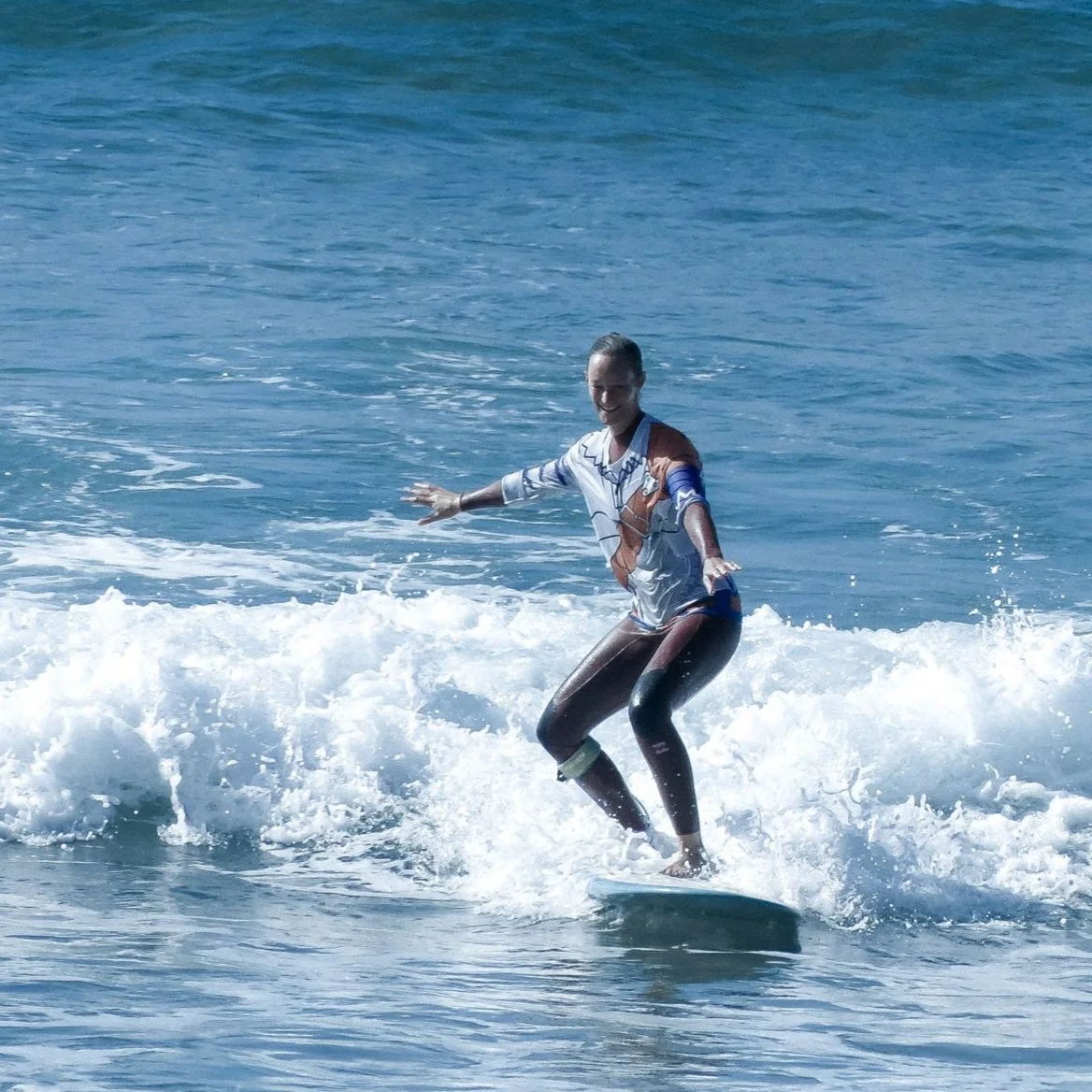 A woman surfing on a wave at the beach, smiling and balancing on her surfboard.