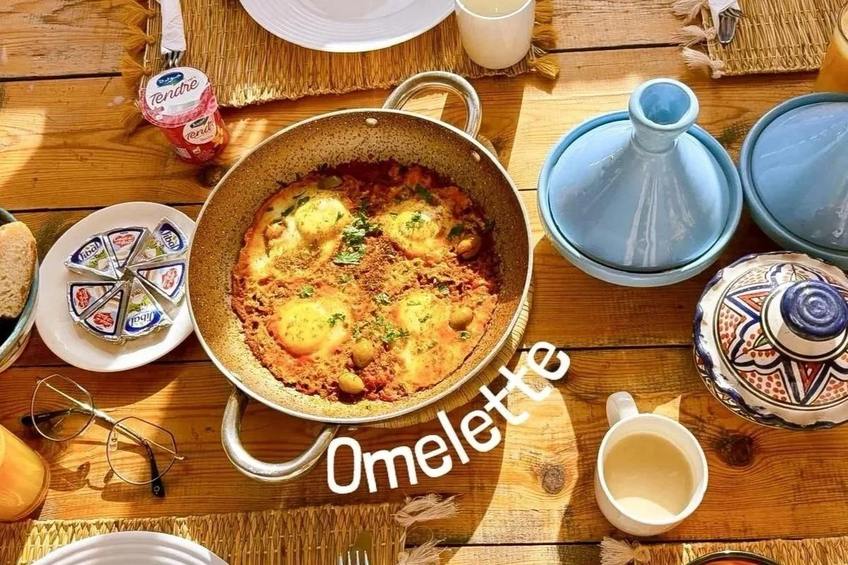 A traditional Moroccan breakfast with a tagine dish, yogurt, honey, bread, glasses, and decorative ceramic pot on a wooden table.